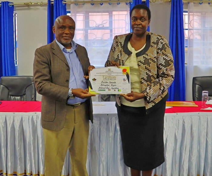 Dr. Vifu Makoti, Ph.D., Patron of the Machakos University Traveling Theatre, presenting award certificate to Prof. Joyce Agalo, the Vice Chancellor of Machakos University.